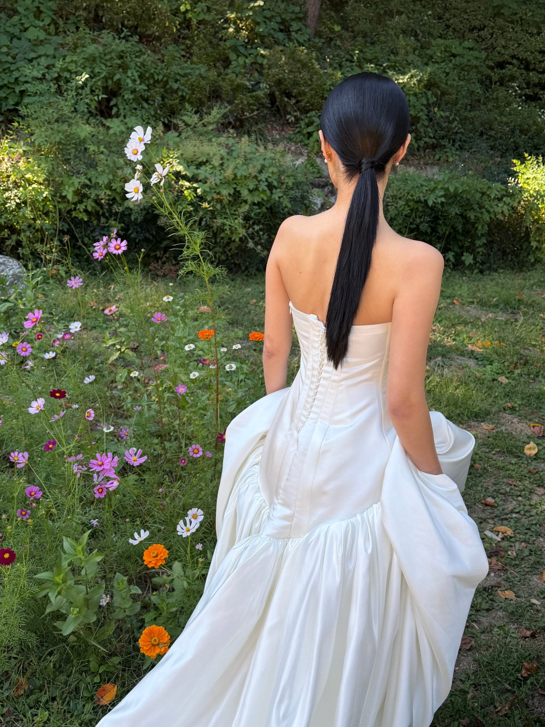 Chaewon seen from behind in a garden of cosmos flowers